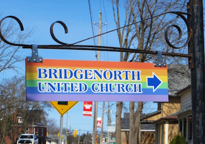 Rainbow coloured sign for Bridgenorth United Church pointing to the right.