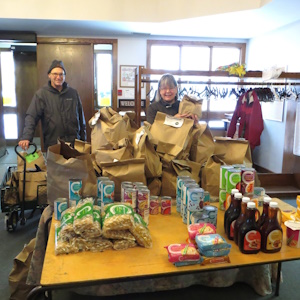 A man and a woman standing behind a table filled with food donations